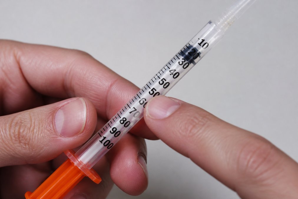 Detailed close-up of a U-100 insulin syringe showing unit markings and graduations with a finger pointing to specific measurement lines, bright clinical lighting