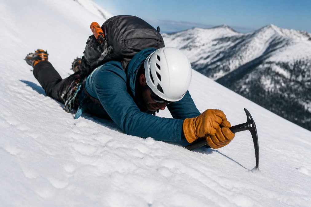 Mountaineer demonstrating how to use an ice axe for self-arrest by digging the pick into a steep snow slope.