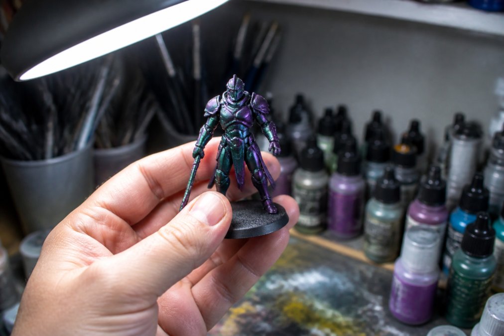 Hobbyist tilting a miniature painted with chameleon paints to reveal a green to purple color shift under a lamp.