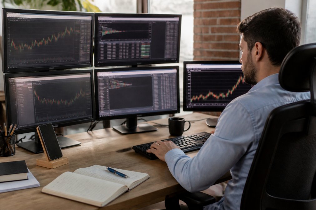 Professional trader at desk with multiple monitors displaying MT5 platform with license key entry dialog visible on screen, natural office lighting