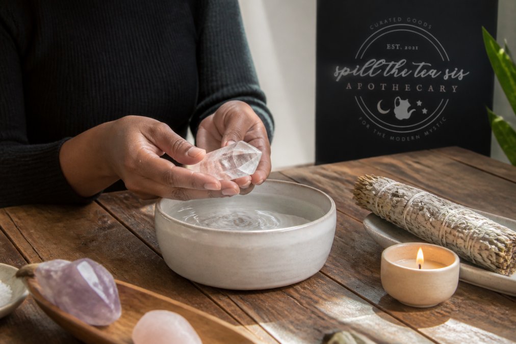 Hands cleansing a clear quartz crystal in water, a step in using spiritual tools for healing rituals.