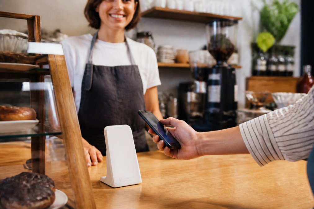 Customer tapping a smartphone on an NFC stand at a cafe checkout counter