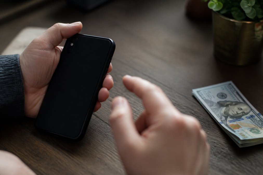 Close-up of a smartphone screen displaying a suspicious text message requesting wire transfer payment with urgent language, hand hovering over phone