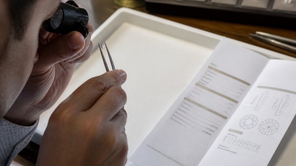 Jeweler using a loupe to inspect a diamond laser inscription next to a grading report on a white tray