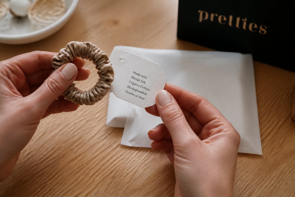 Hands holding a biodegradable hair tie and materials tag to help you learn how to verify ethical hair accessory brands