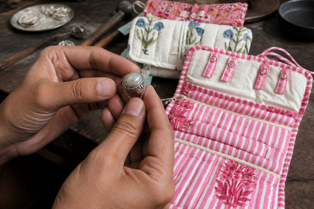 Close-up of hands holding an artisanal silver ring, with a jeweler's workspace in soft focus behind, showing tools and polished pieces