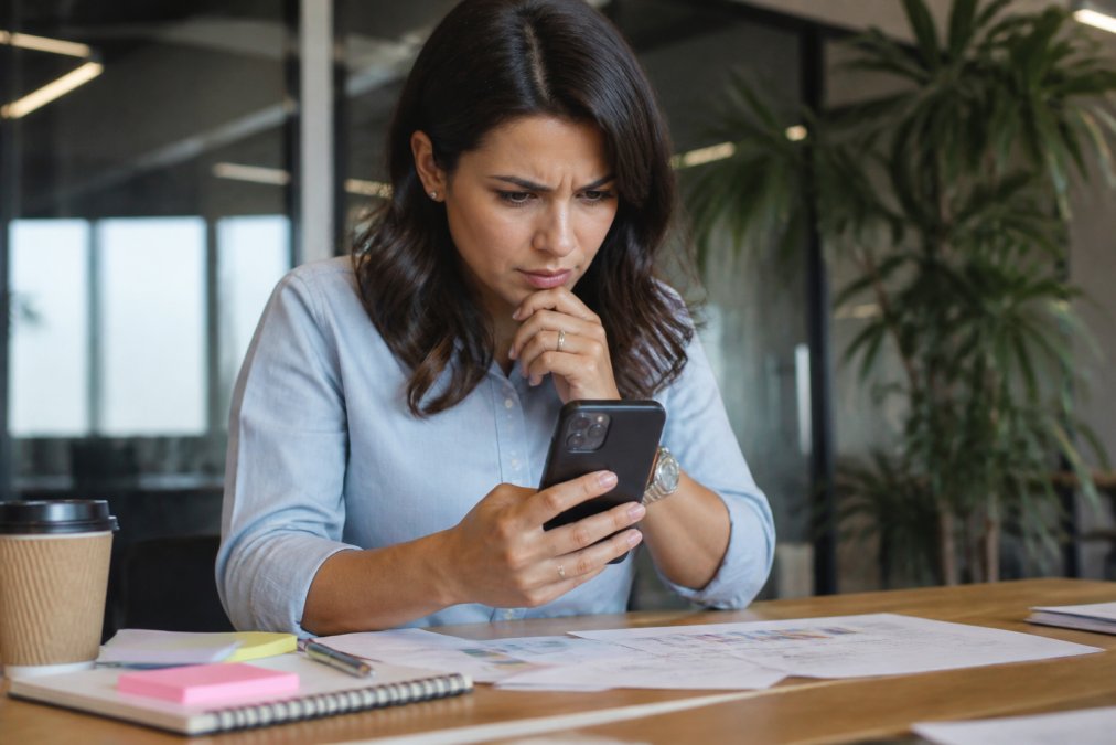 Marketing professional checking a smartphone screen to verify influencer engagement in a bright office.
