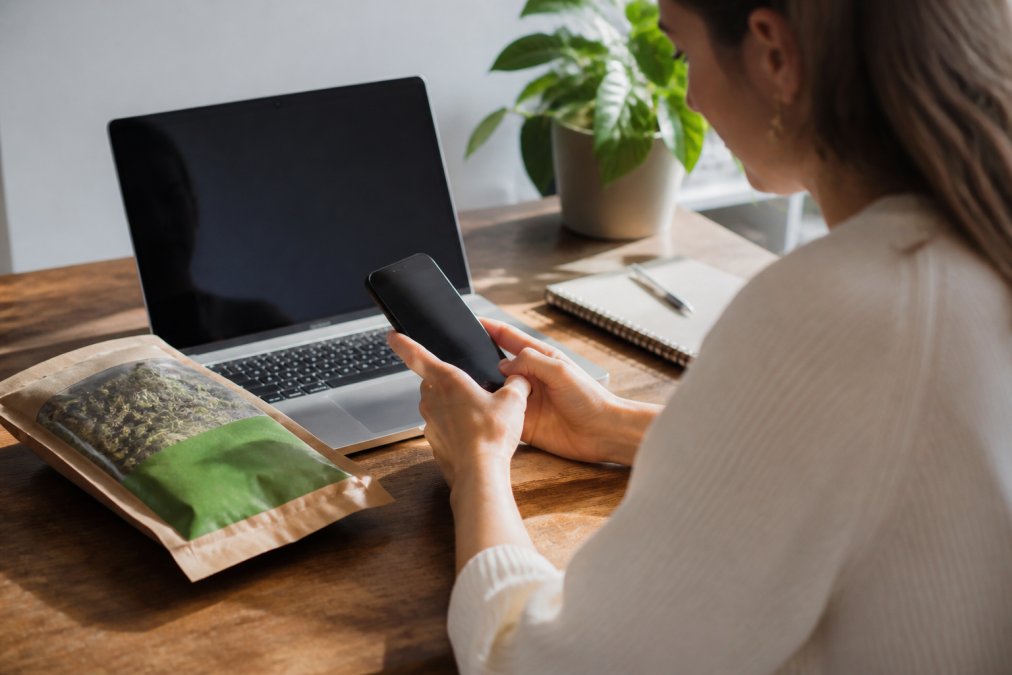 Person using a smartphone to search the USDA Organic Integrity Database with a package of organic food visible on the desk nearby, natural office lighting