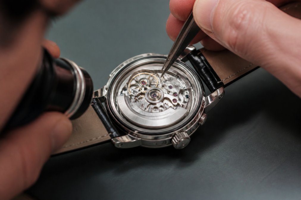 Horologist examining the internal movement and caliber of a luxury watch through an open caseback, showing detailed mechanical components and escapement under magnification