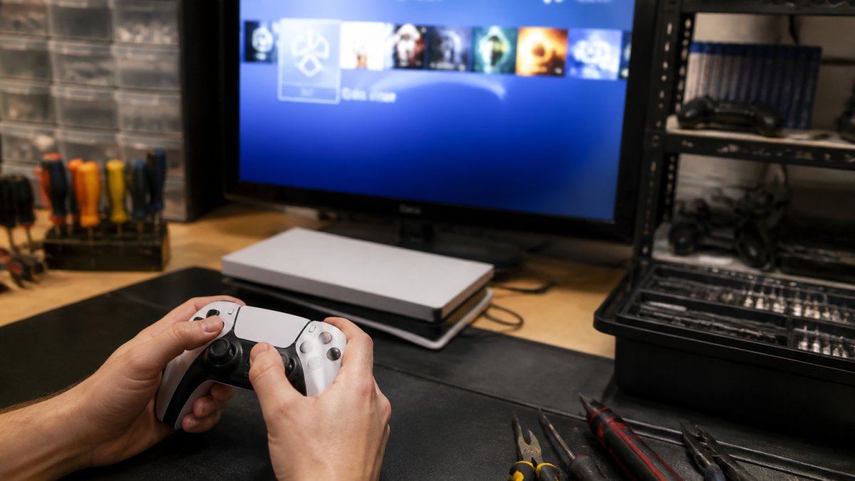 Gamer's hands holding a controller while testing button responsiveness on a refurbished console, with a TV screen displaying the game menu in the background