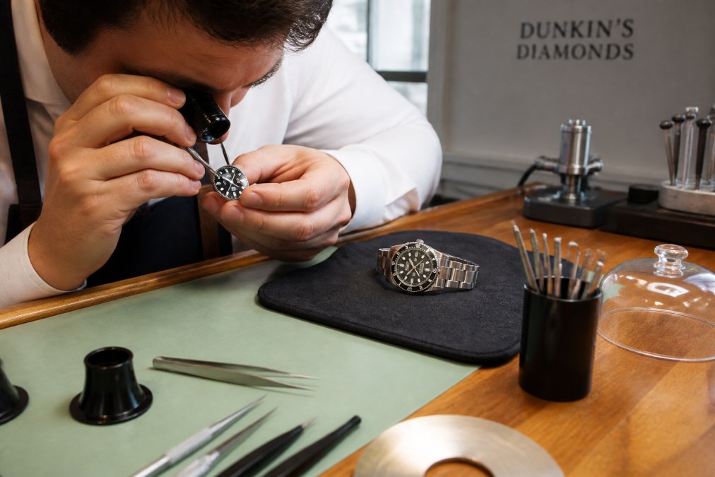 Jeweler using a magnifying loupe to inspect the dial and lens of a luxury wristwatch on a workbench