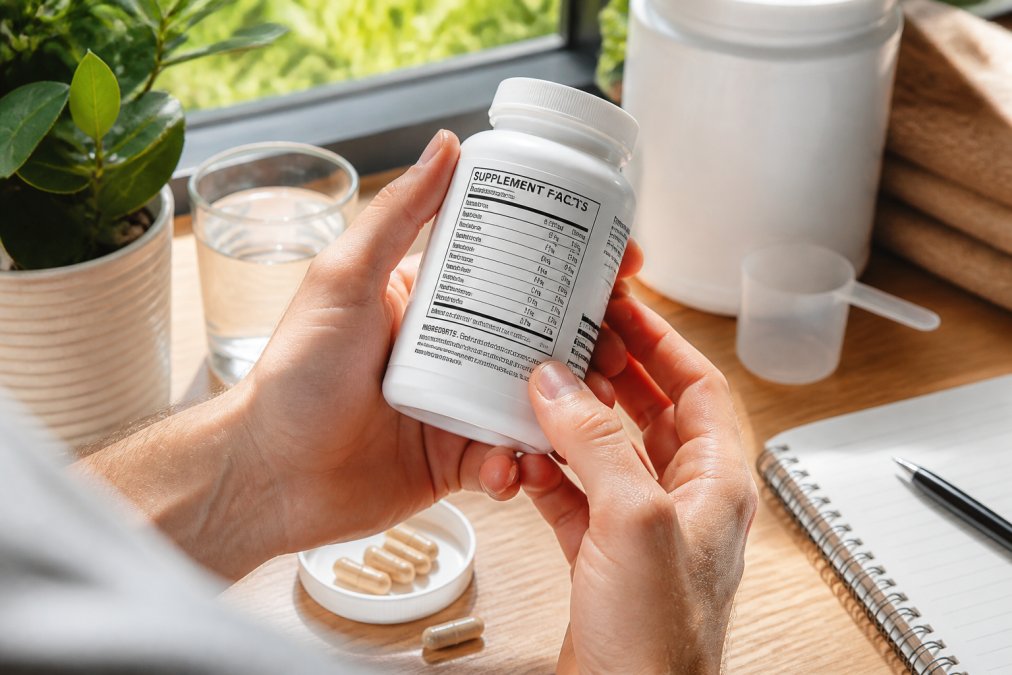 Close-up of hands holding a supplement bottle and examining the detailed ingredient list and supplement facts panel in natural daylight near a window