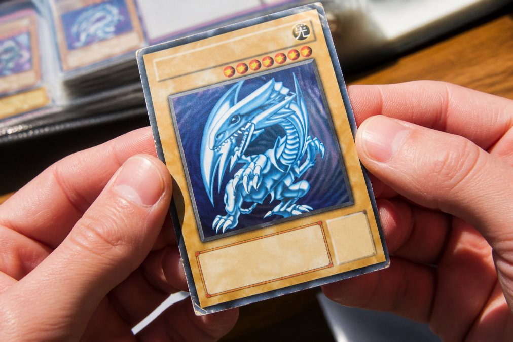 Close-up of hands holding a trading card under bright natural light, showing surface texture, centering alignment, and edge wear details clearly visible