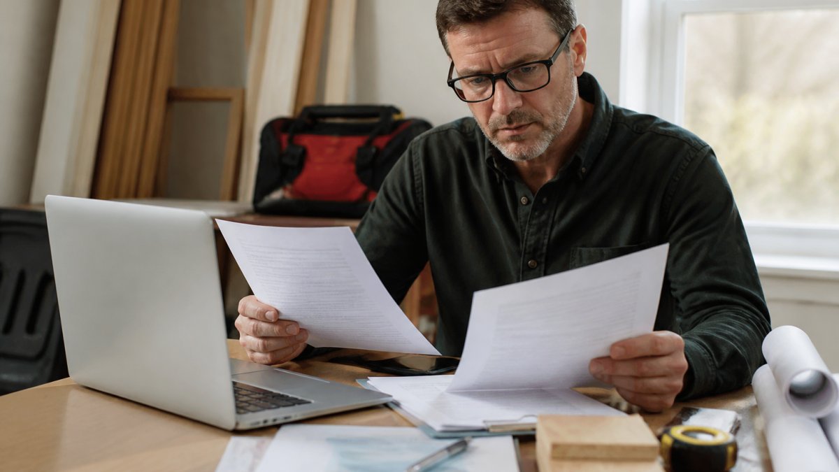 Professional homeowner reviewing contractor credentials and insurance documents at desk with laptop and paperwork