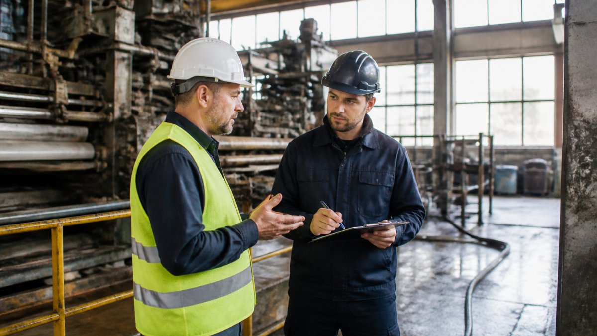 Facility manager consulting with vet industrial cleaning contractors in an industrial site with heavy machinery.