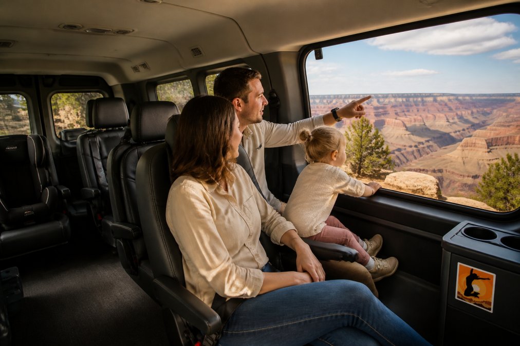 Family of four with a toddler in a comfortable Ford Transit van, child looking out window at canyon landscape, parent pointing toward viewpoint, flexible seating arrangement visible