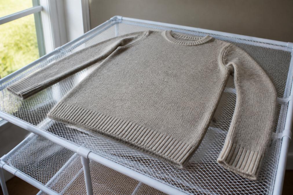 An alpaca sweater laid flat on a mesh drying rack in natural light, showing proper shape retention and even air circulation