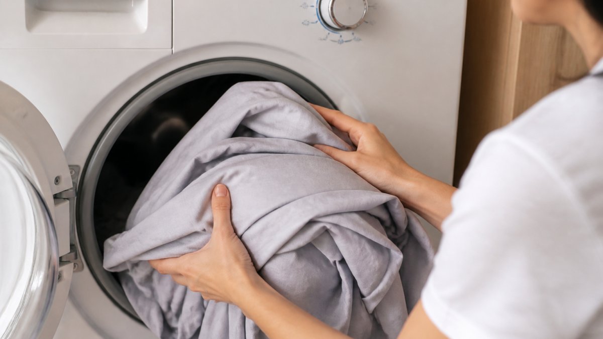 Close-up of hands placing bamboo viscose sheets into a washing machine with cold water setting visible on the dial
