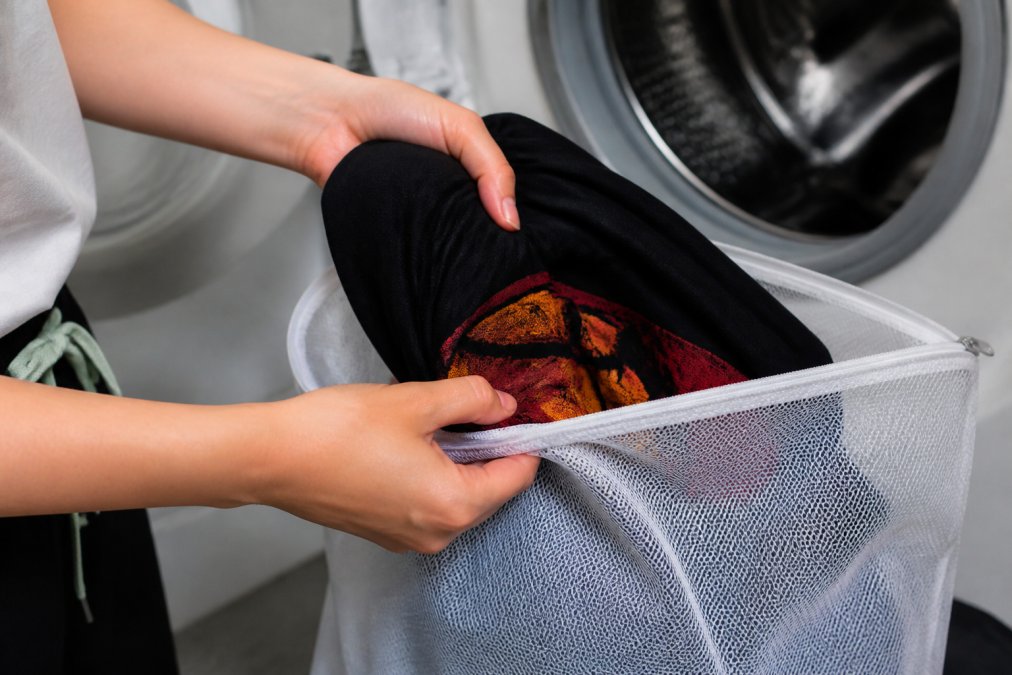 Close-up of hands carefully turning a graphic tee inside out, showing the vibrant print facing inward before placing it into a mesh laundry bag for protection