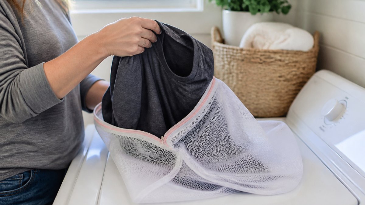 Hands turning a graphic tee inside out to place it into a mesh laundry bag before you wash graphic tees.