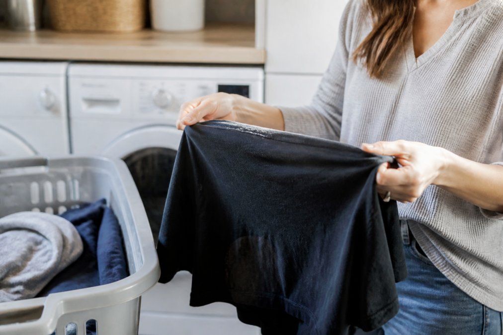 Close-up of hands turning a graphic t-shirt inside out next to a laundry basket in a bright home laundry room