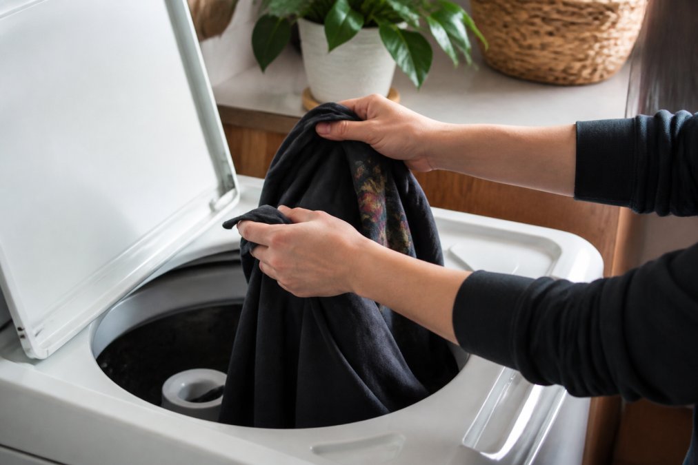 Hands turning a graphic tee inside out over a washing machine, showing the printed design facing inward with natural kitchen lighting