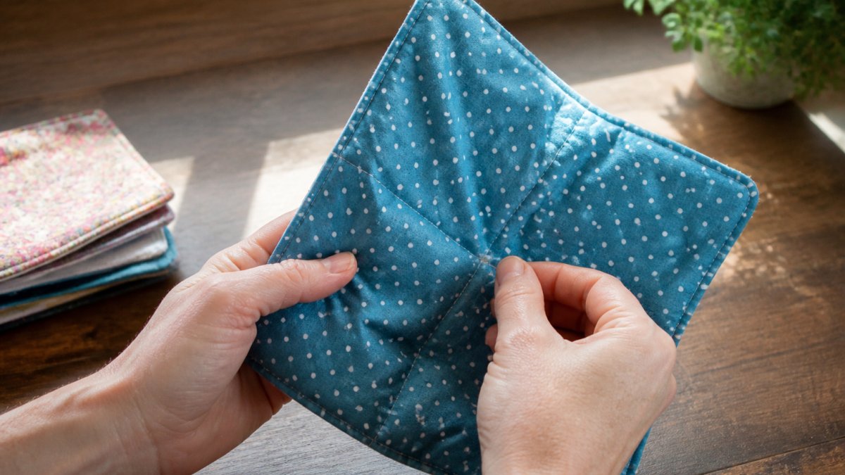 Hands inspecting a fabric bowl cozy for loose threads and stains before washing