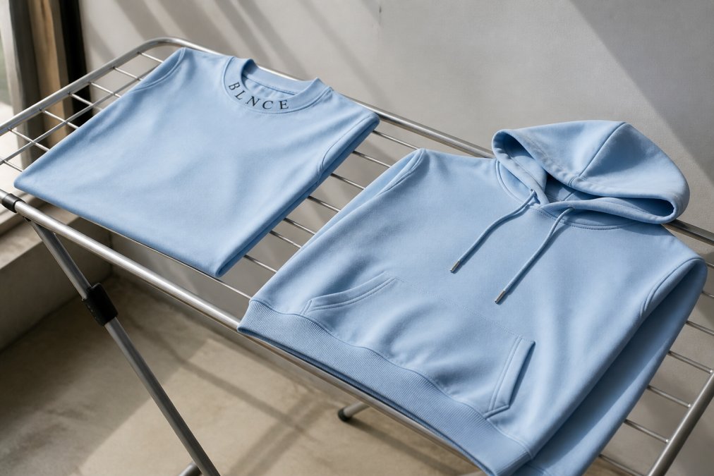 Heavyweight cotton tees and hoodies laid flat on a drying rack in natural light, showing proper air-drying technique with garments smoothly positioned to maintain shape