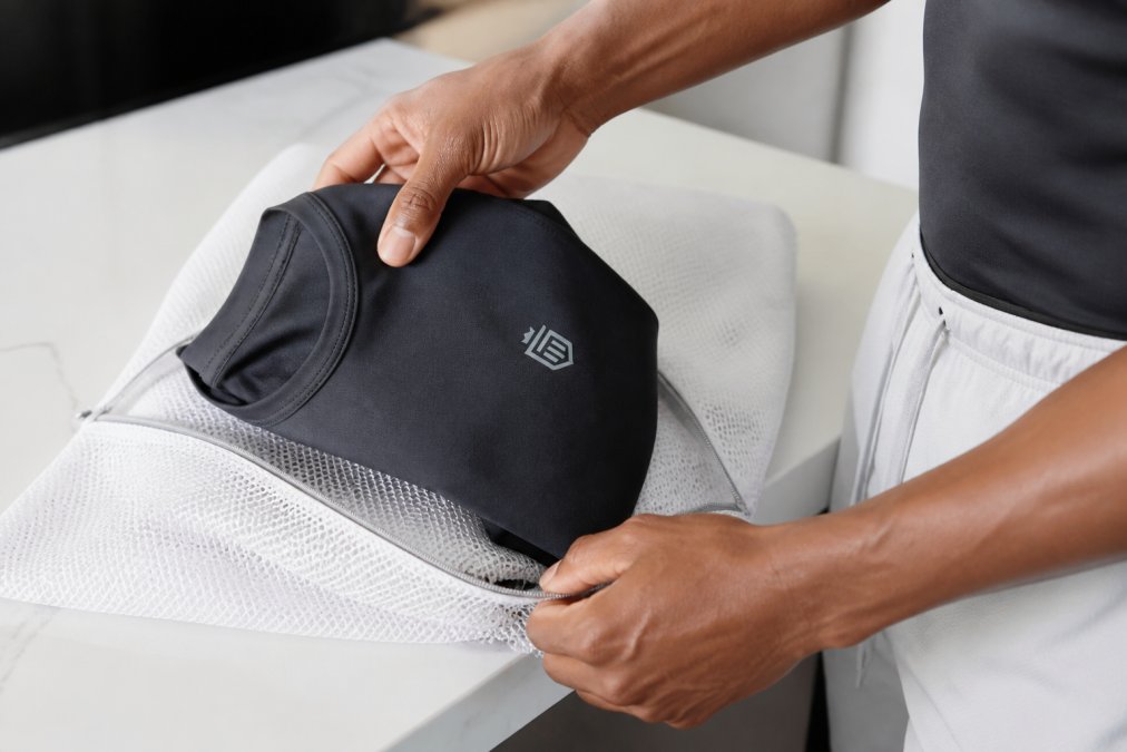 Close-up of hands placing moisture-wicking athletic clothes into a mesh laundry bag, with natural light illuminating the fabric texture and mesh material