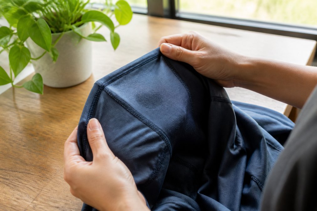 Hands carefully inspecting a performance fabric garment inside-out under bright natural light, checking seams and a small water stain before washing