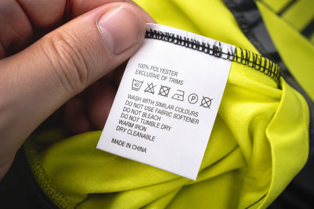 Close-up of a garment care label on hi-vis work clothing showing washing instructions and fabric composition details