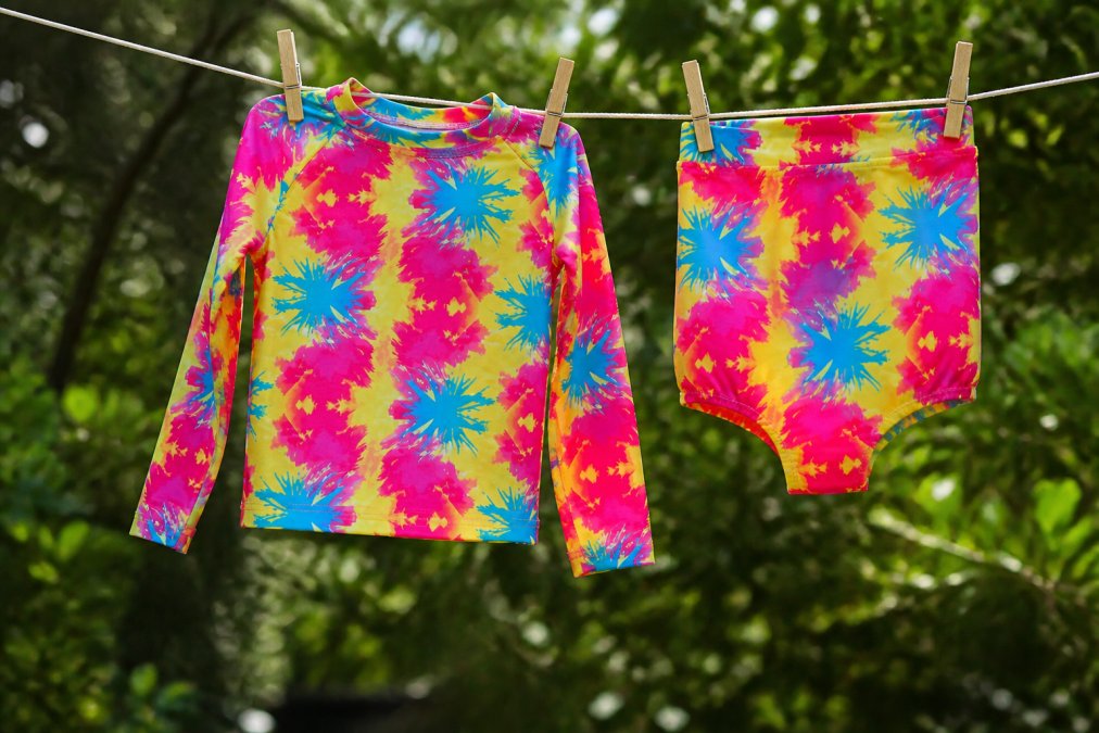 Colorful UPF swimwear hanging on a clothesline in natural outdoor light with green foliage in soft-focus background, showing proper air-dry technique