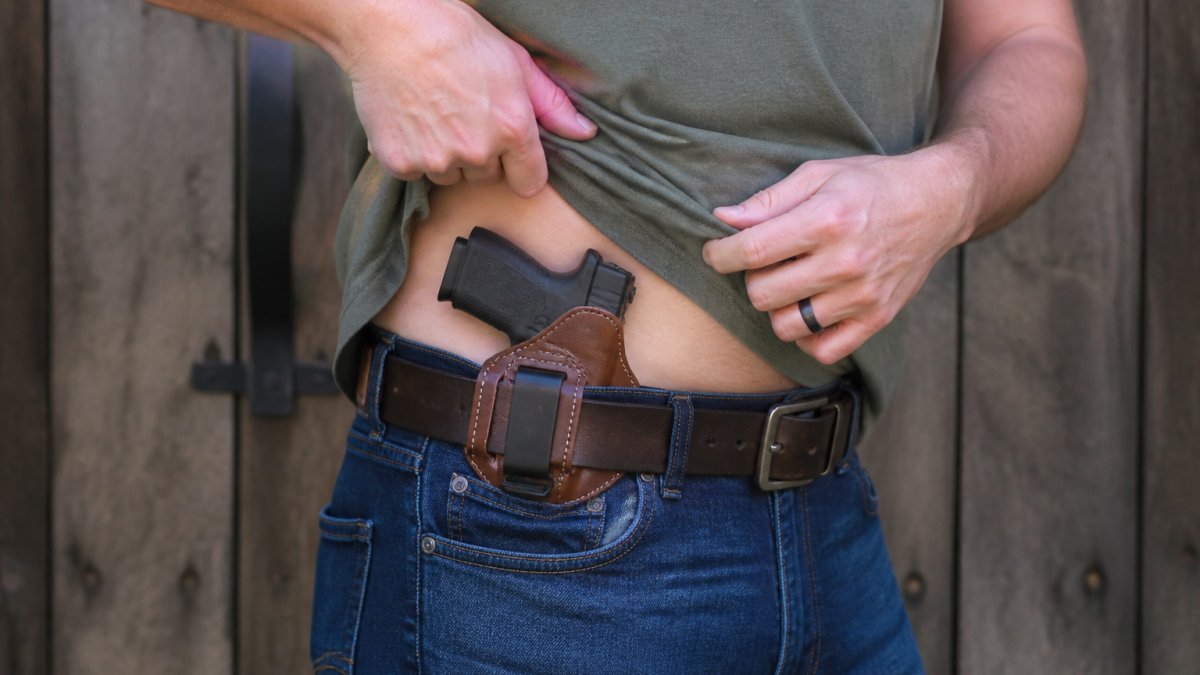 Person demonstrating proper IWB leather holster positioning at waistband, showing correct ride height and cant angle for comfortable concealed carry with natural lighting