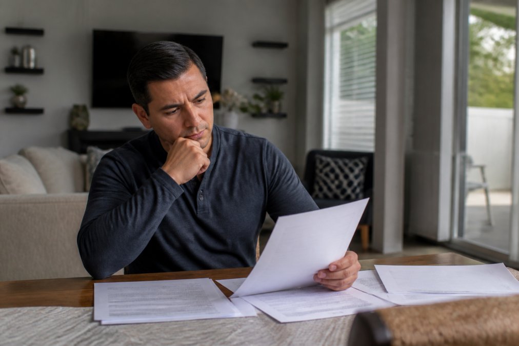 Homeowner reviewing multiple competing offers in their home, looking thoughtful while holding offer documents with natural afternoon light