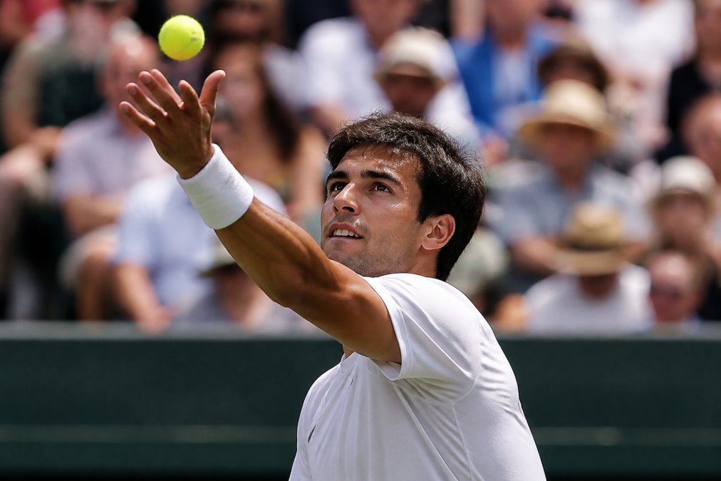Focused tennis player with determined expression during serve in high-pressure match moment, showing composure and concentration with natural court lighting