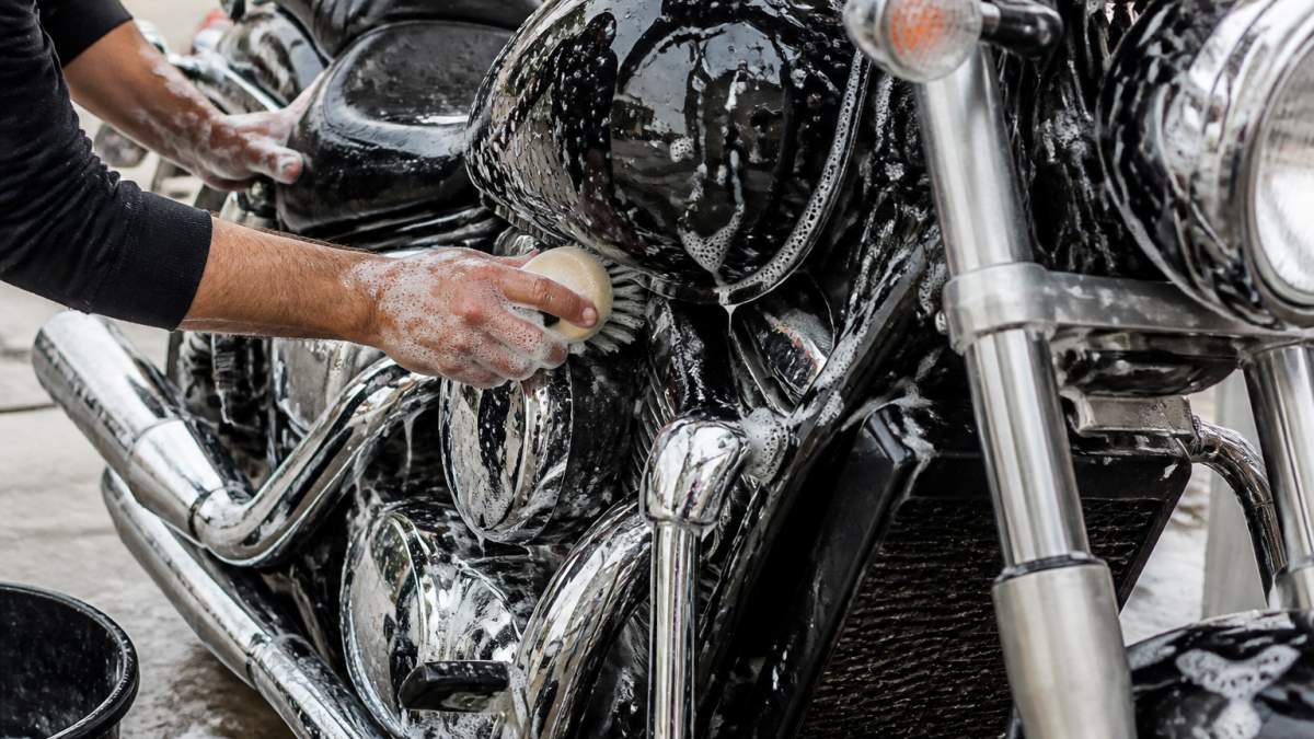 Infographic showing the detailed cleaning process for motorcycle winterization using soapy water and brushes.