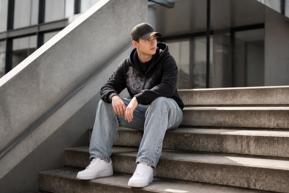 Ung voksen i en oversized HTT streetwear-hoodie og grafisk T-shirt med sneakers og kasket i et urbant miljø.