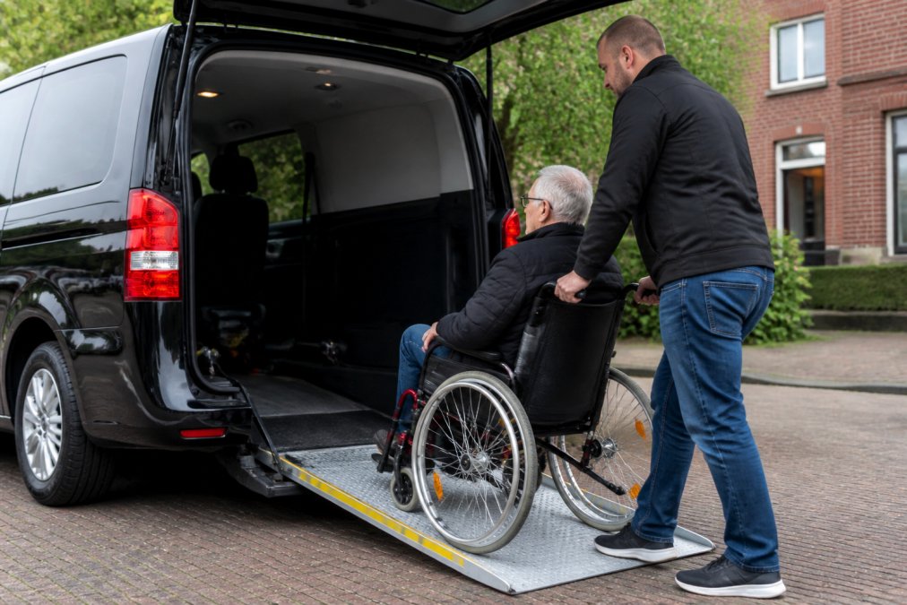 Gecertificeerde chauffeur helpt passagier in rolstoel voorzichtig in een aangepaste taxi met oprijplaat uitgebreid, waarbij beide partijen zich concentreren op veilige beweging en correcte positionering
