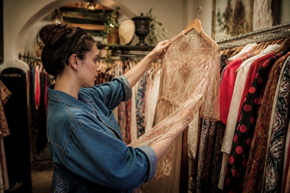 Person prüft die Qualität eines Vintage-Kleidungsstücks als nachhaltige second hand alternative in einem Laden.