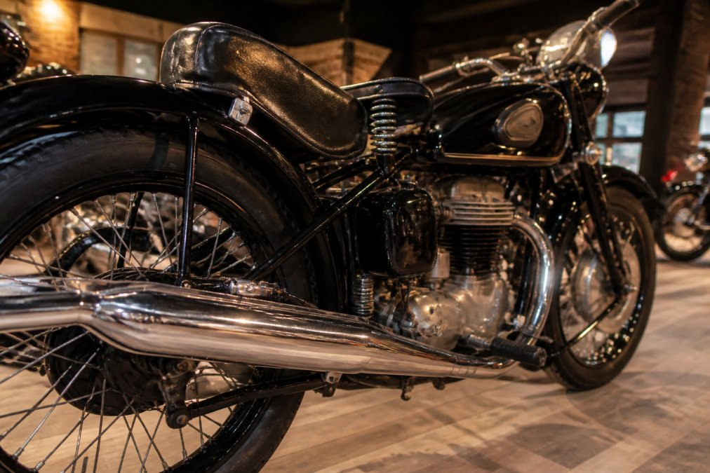 Close-up van een gerestaureerde Husqvarna motorfiets in een showroom, glanzend chroom op de uitlaat, warme spots op het zwarte frame en lederen zadel