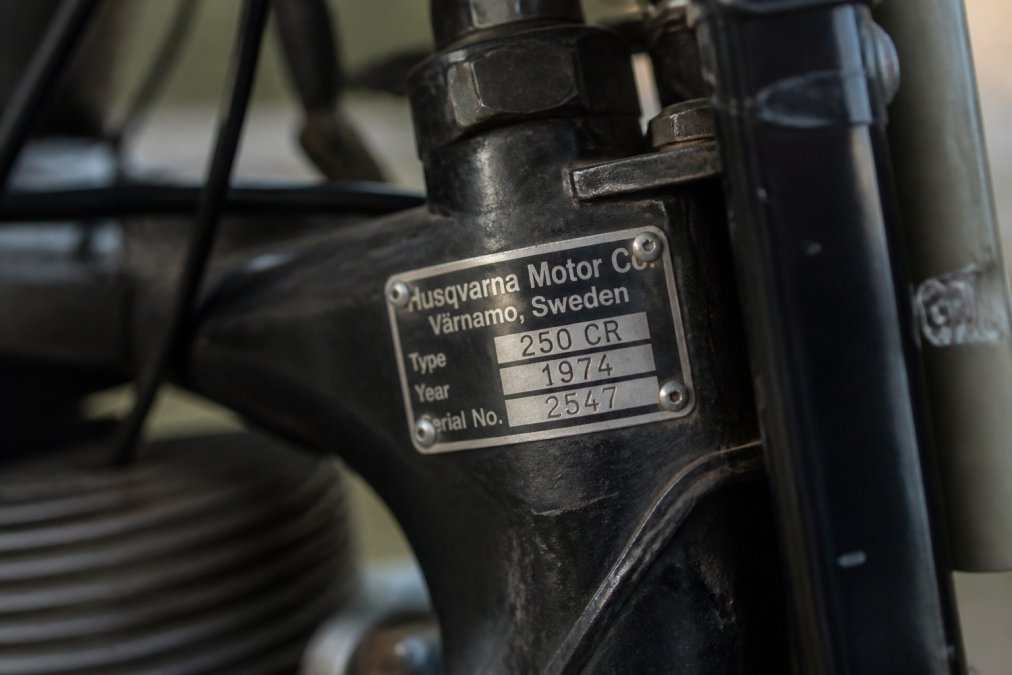 Close-up van een Husqvarna typeplaatje met zichtbare modelnummer, productiejaar en serienummer op het motorframe onder natuurlijk licht
