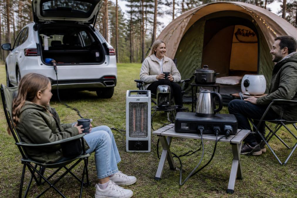 Family camping at tent with electrical appliances plugged into V2L socket, heat source and light in natural daylight