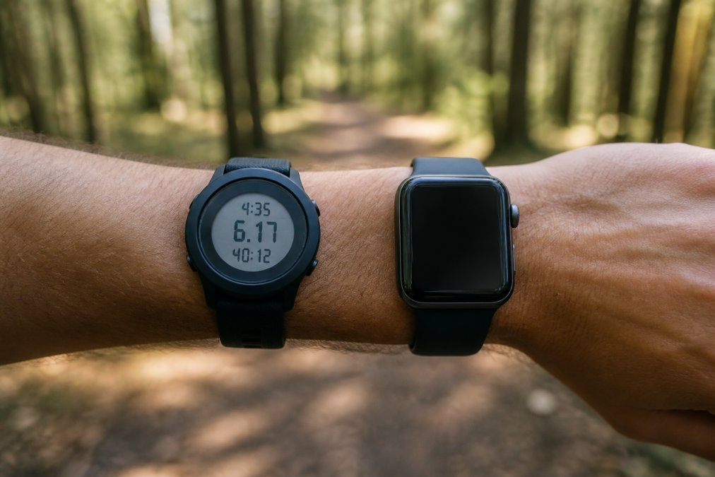 Close-up of two different watches on a wrist during an outdoor run, one with a minimalist sport design and one with a bright touchscreen display, blurred forest path in background