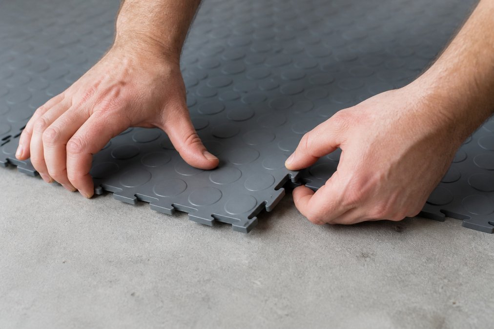 Hvorfor vælge Fortelock PVC gulve systemer 2 Nærbillede af hænder der forbinder to grå PVC-fliser med klik-systemet, viser den enkle og hurtige installationsproces uden værktøj eller lim