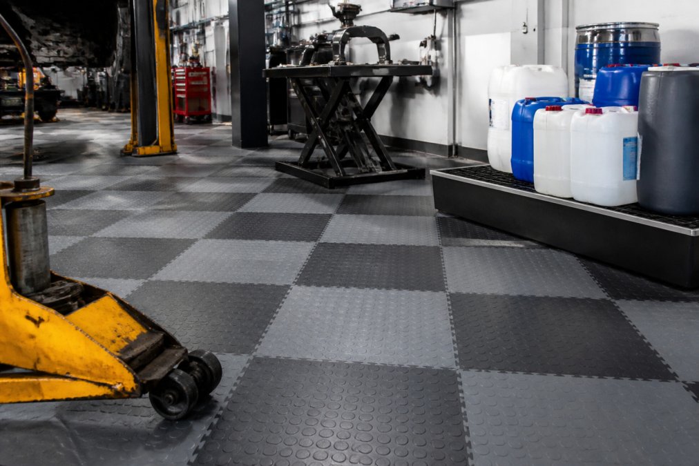 Hvorfor vælge Fortelock PVC gulve systemer 3 Et professionelt værksted med tungt udstyr, værktøjer og kemikalitanke på grå og sorte PVC-gulvfliser, der viser modstandsdygtighed og praktisk anvendelse i industrielt miljø