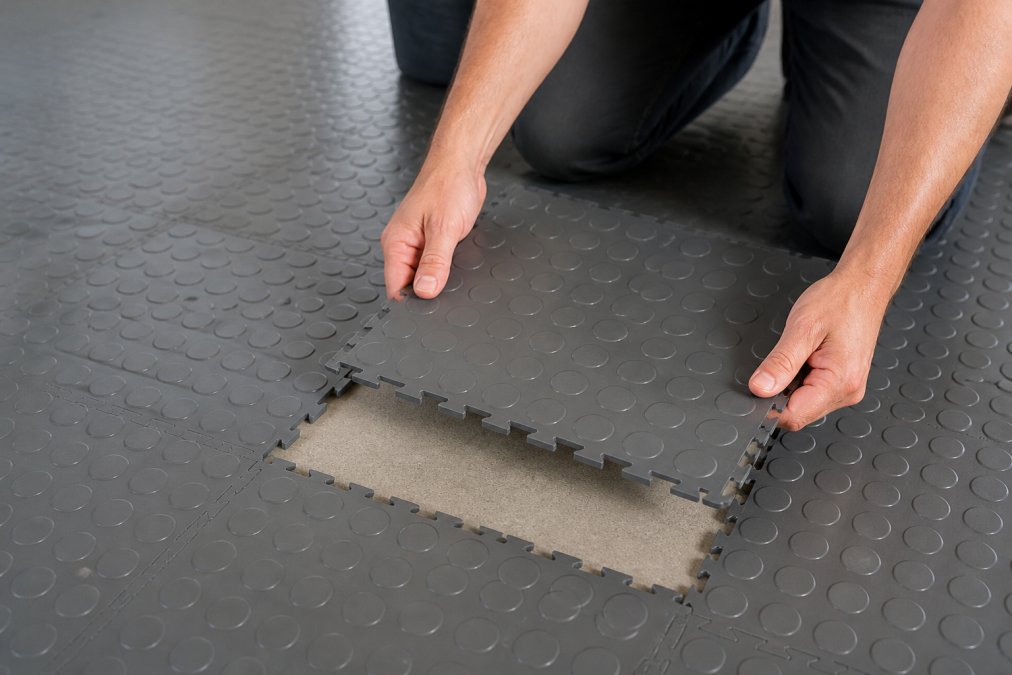 Hvorfor vælge PVC-fliser til garage 3 Trin-for-trin demonstration af, hvordan man løsner og udskifter en enkelt PVC-garagegulvflis ved hjælp af kliksystemet, viser hænder, der arbejder med fliserne uden værktøj