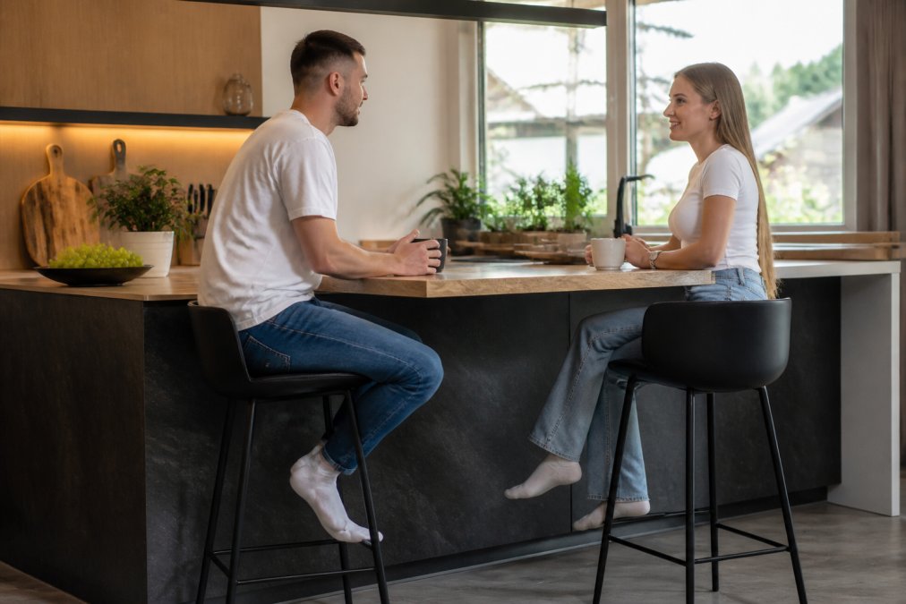 Lidé sedící u kuchyňského ostrůvku, kde dostatečná hloubka pracovní desky zajišťuje pohodlí pro nohy.