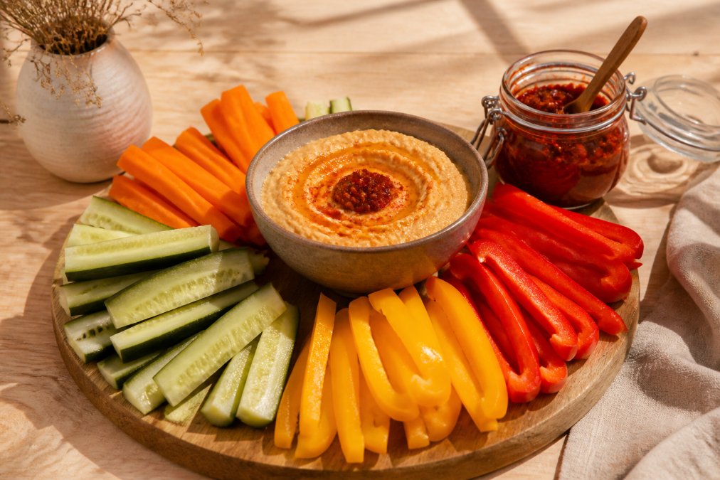 Infographie présentant des idées de collations saines à la harissa avec des légumes crus et du houmous épicé.