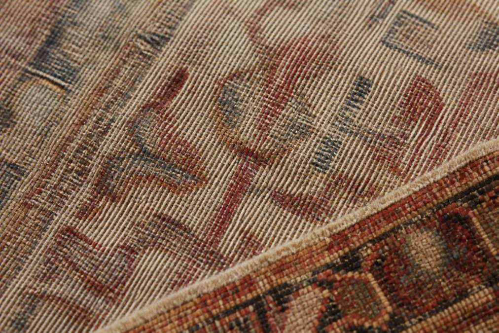 Close-up of antique Persian rug back showing hand-spun warp and weft threads with visible irregularities and natural color variations in wool fibers under soft studio lighting
