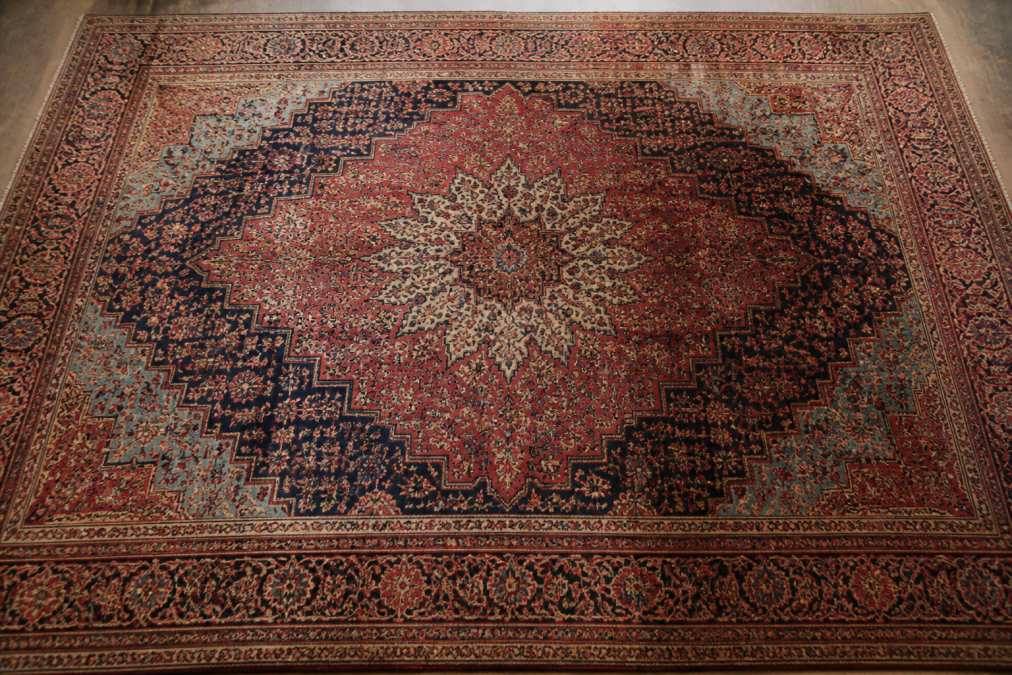 Detailed overhead view of antique Persian rug displaying traditional medallion pattern with intricate floral borders, showing natural abrash color variations in red and blue fields with visible oxidization darkening in certain areas